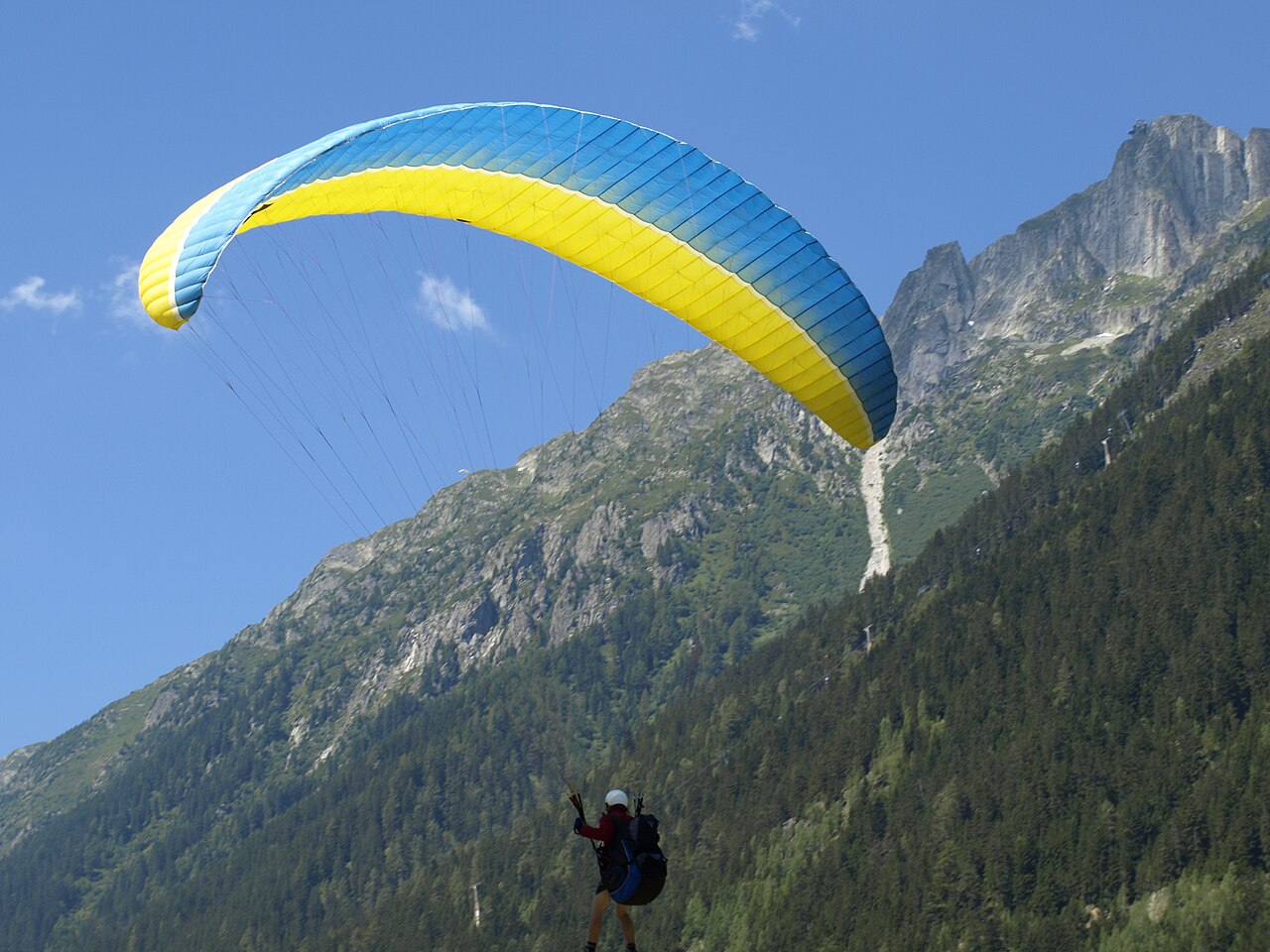 Parapente jaune et bleu devant des montagnes